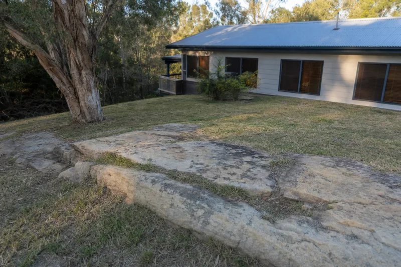 A pale sandstone rock shelf breaking through the lawn of a sloping backyard below a house — rock excavation, Central Coast. Illustrative example.
