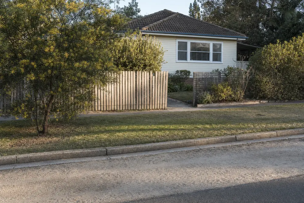 A grassed nature strip and kerb in front of a weatherboard cottage with no driveway crossing — excavation, Central Coast. Illustrative example.